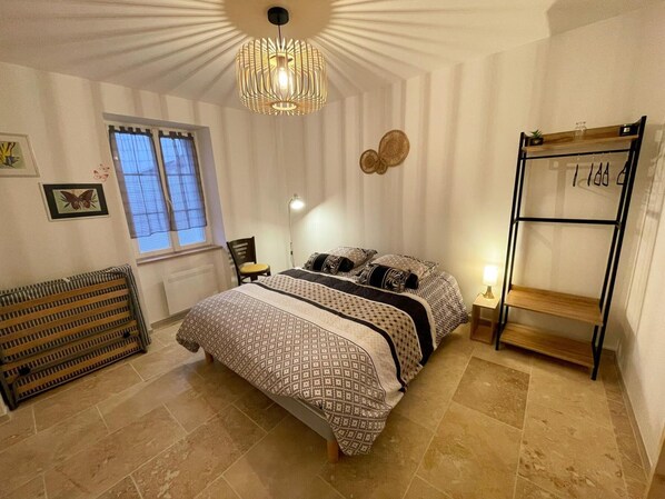 A bedroom with a bed, a radiator, a window, a wall clock, and a shelf.