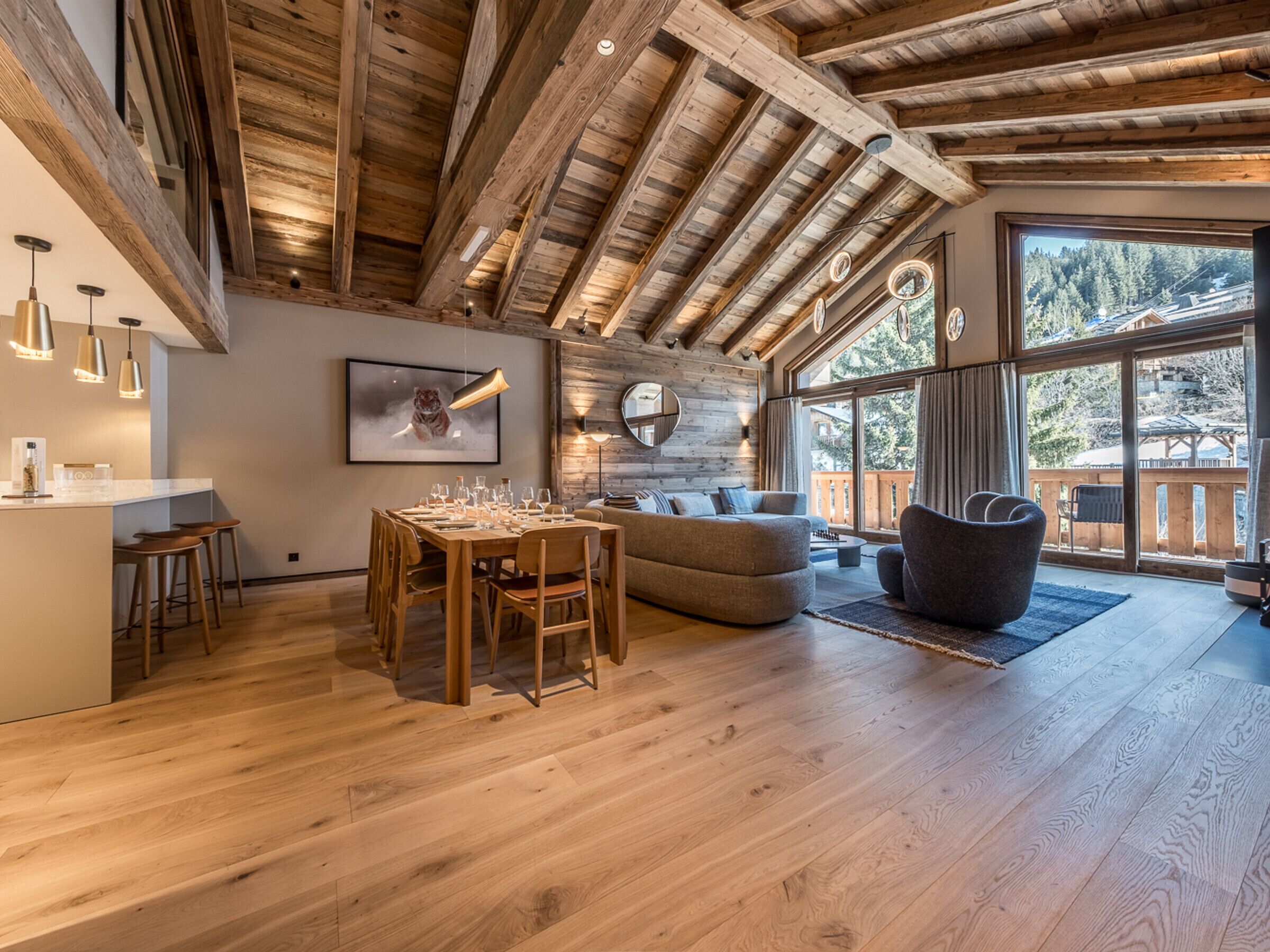 Un'ampia stanza con soffitto in legno, un'area da pranzo con tavolo e sedie, un divano e un'ampia finestra con vista sull'esterno.