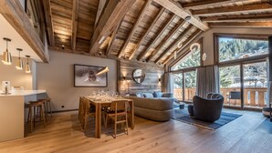 Um quarto espaçoso com teto de madeira, sala de jantar com mesa e cadeiras, sofá e uma grande janela com vista para o exterior.