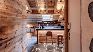 Une cuisine rustique avec des poutres en bois, un sol en pierre et un coin bar avec des tabourets.