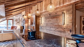 Une cuisine moderne avec un plan de travail en marbre foncé, des murs en bois et des luminaires suspendus.