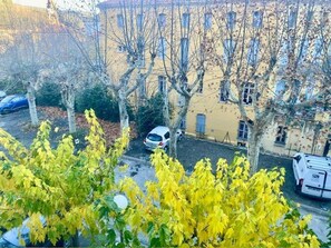 Un quartiere residenziale con un'auto bianca parcheggiata, alberi con foglie gialle e un edificio con molte finestre.