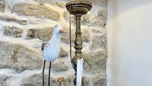 A decorative bird sculpture on a stand, a clear glass vase with pebbles, and a stone wall background. - Renovated house in town center, 3 bedrooms, near shops (Groix)