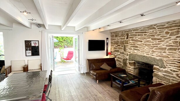 A spacious living area with a stone fireplace, a dining table with chairs, and a comfortable seating arrangement. - Renovated house in town center, 3 bedrooms, near shops (Groix)