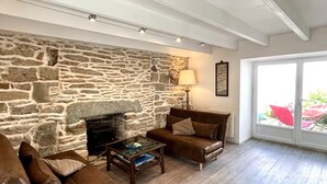 A living room with a stone fireplace, leather sofas, a coffee table, and a view through a large window. - Renovated house in town center, 3 bedrooms, near shops (Groix)
