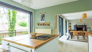 A modern kitchen with a wooden countertop, a dining area with chairs, and a view of greenery outside.
