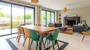 A spacious living room with a dining area, large windows, a fireplace, and a balcony.
