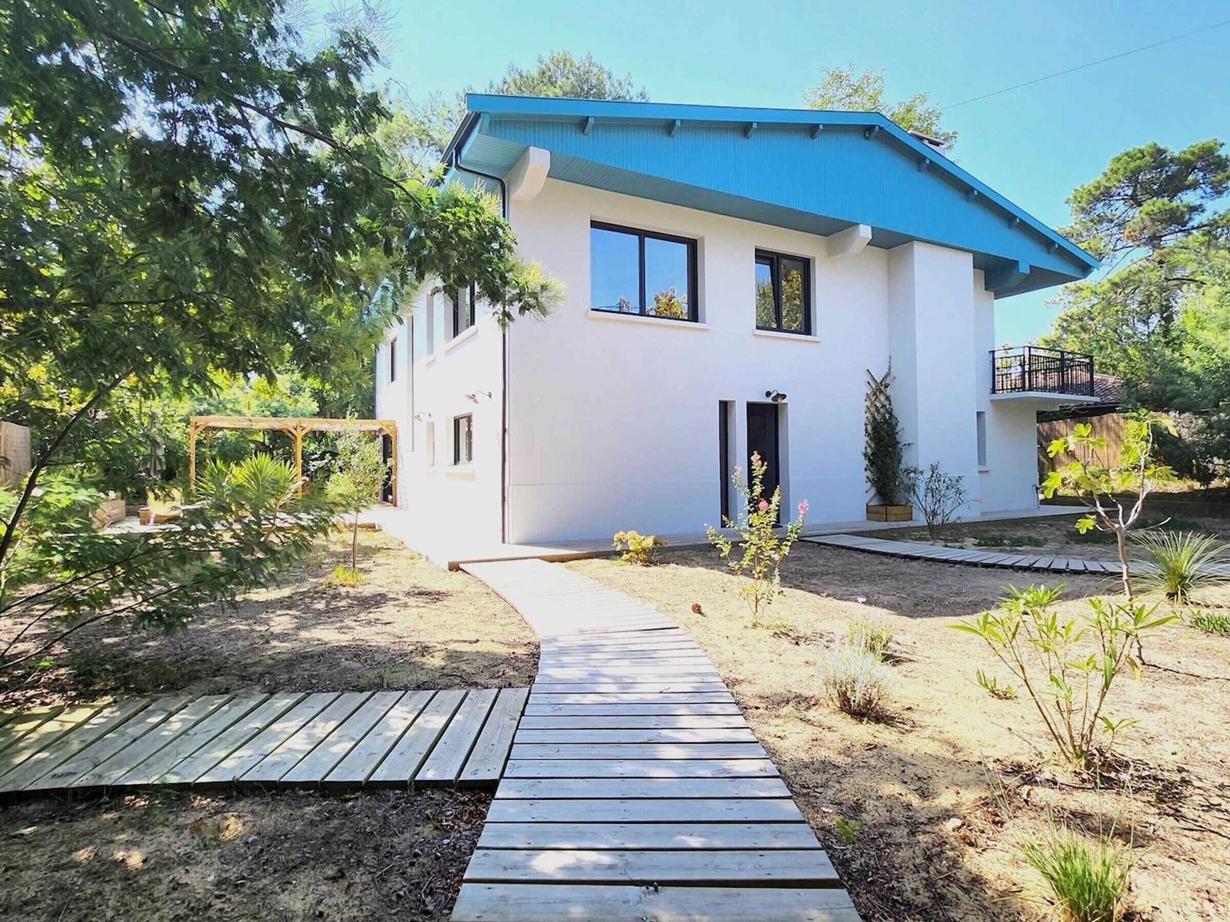 A modern two-story house with a blue roof, a wooden deck, and a garden with various plants.