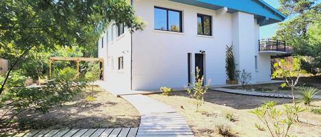 A modern two-story house with a blue roof, a wooden deck, and a garden with various plants.