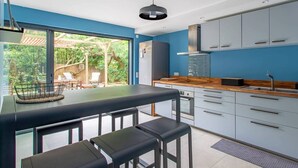 A modern kitchen with a large island, bar stools, and a view of a lush garden.