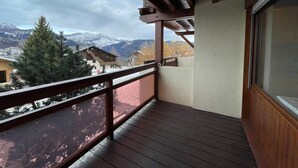 Ein Balkon mit Holzboden und Geländer, mit Blick auf eine Berglandschaft mit schneebedeckten Gipfeln und herbstlich gefärbten Bäumen.