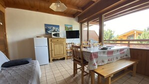 Ein gemütliches Blockhauszimmer mit Holzbalkendecke, einem Esstisch für zwei Personen, einem weißen Kühlschrank, einer Mikrowelle und einem Fernseher.
