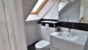 Een moderne badkamer met dakraam, witte inrichting en zwarte tegels.