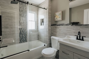 Un baño moderno con cabina de ducha de vidrio, inodoro blanco y lavamanos con grifo negro.