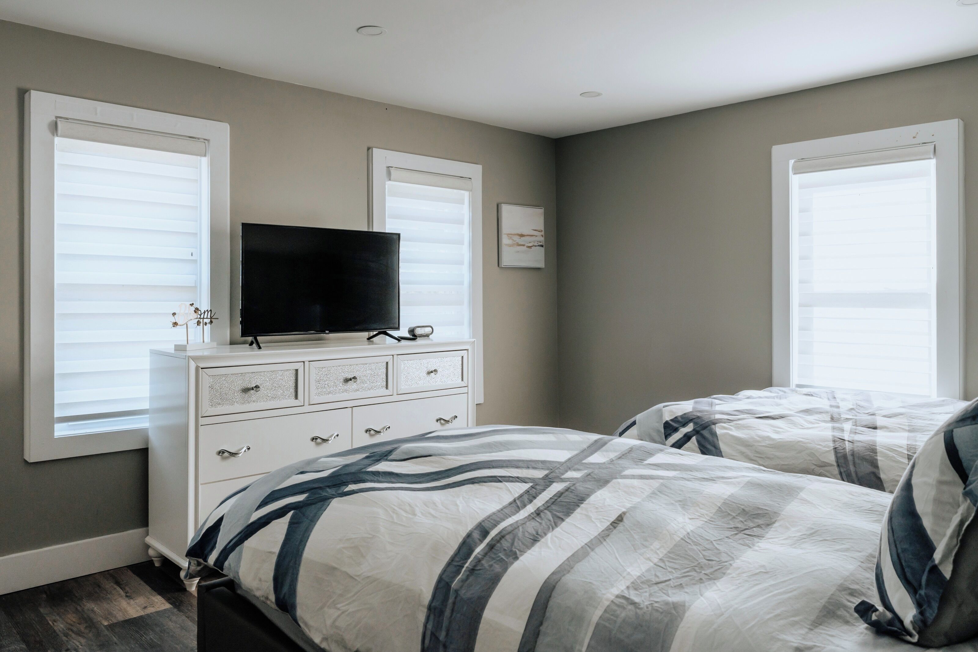 A bedroom with two beds, a dresser, a television, and a window with blinds.