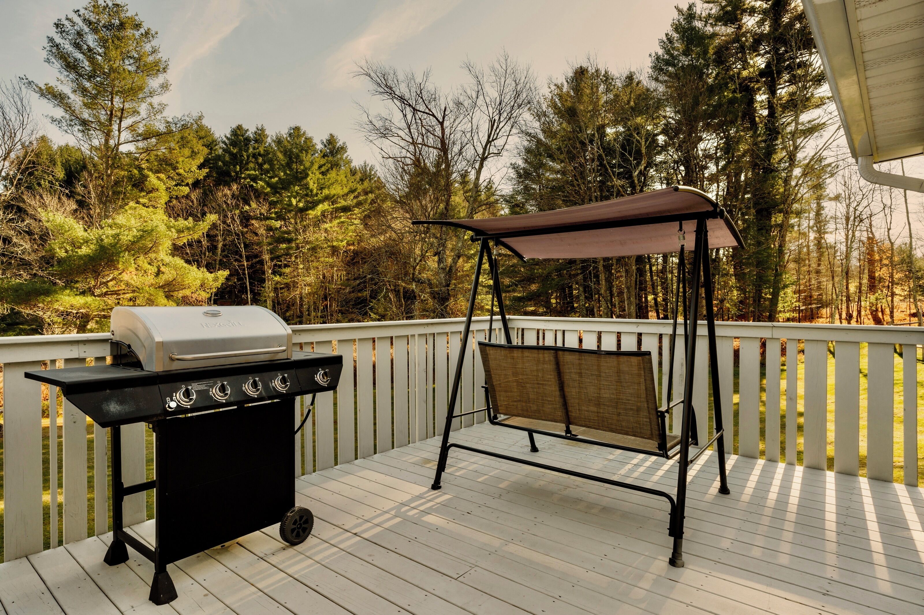 A deck with a barbecue grill and a swing chair.