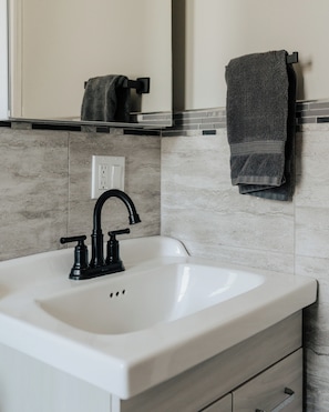 Un baño con un lavamanos blanco, grifo negro y un perchero con una toalla.