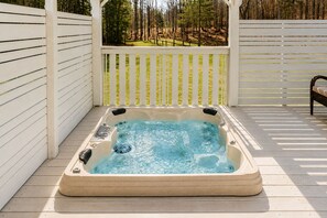 Ein Whirlpool auf einer Holzterrasse mit einem weißen Zaun und Bäumen im Hintergrund.