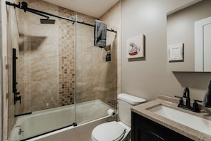 Un baño moderno con ducha de vidrio, inodoro blanco y lavamanos con encimera de granito.