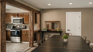 Une cuisine moderne avec des meubles en bois, un four en acier inoxydable et un coin repas comprenant une longue table et des chaises.