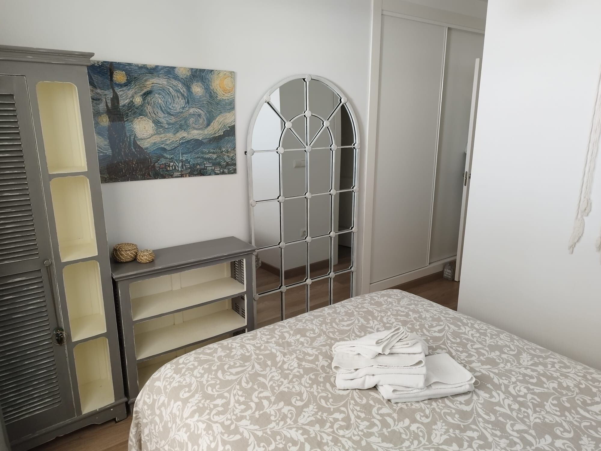 Un dormitorio con cama, armario con espejo, un cuadro en la pared y una mesita de noche con lámpara.