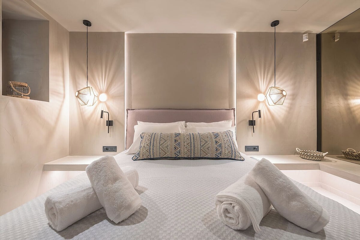 A modern hotel room with a large bed, two bedside tables, and a headboard.