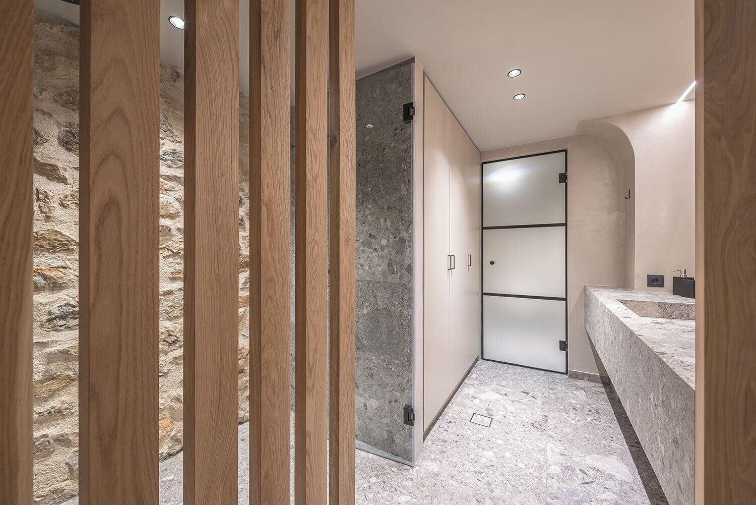 Ein modernes Badezimmer mit Steinwand, Holzabtrennung und Marmorplatte.