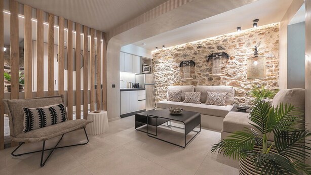 Ein modernes Wohnzimmer mit einer Wand aus Stein, einer Sofagarnitur, einem Couchtisch und einem Sessel mit gemustertem Kissen.