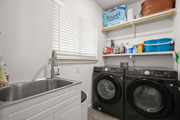 A laundry room with a sink, two front-loading washers, and shelves with laundry supplies. - Exquisite modern retreat 2 blocks from Lake Austin & Nature (Austin)