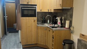 Une cuisine compacte avec des meubles en bois, un four à micro-ondes encastré, un évier et une poubelle.