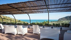 A covered outdoor seating area with white wicker chairs and a view of the sea.