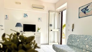 A living room with a sofa, a TV, a plant, and artwork on the walls.