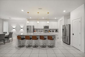 A modern kitchen with a central island, bar stools, stainless steel appliances, and pendant lighting. - Luxurious 15-Bedroom Villa with Pool near Disney! (Kissimmee)