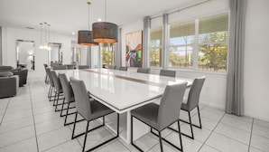 Un espace de restauration moderne, doté d’une longue table, de chaises, de luminaires suspendus et de grandes fenêtres.