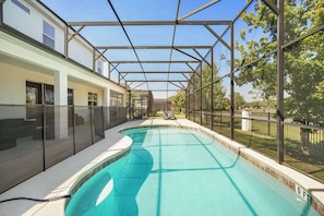 A swimming pool with a glass enclosure, surrounded by a building with large windows and a covered patio area. - Luxurious 15-Bedroom Villa with Pool near Disney! (Kissimmee)