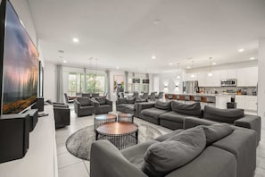 A modern living room with a large flat-screen TV, grey sofas, and a coffee table. - Luxurious 15-Bedroom Villa with Pool near Disney! (Kissimmee)