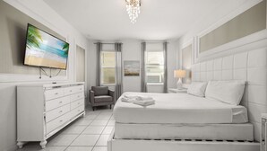 Une chambre à coucher avec un grand lit, un téléviseur fixé au mur, une commode et une chaise.