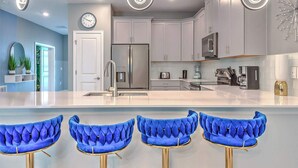 Una cocina moderna con armarios blancos, electrodomésticos de acero inoxidable y una isla central con taburetes de bar.