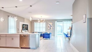 Una cocina amplia con una isla central, una zona de comedor con sillas azules y una sala de estar con sofá azul.