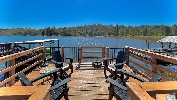A wooden deck with two Adirondack chairs facing a lake, surrounded by a metal railing.
