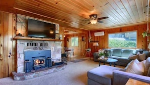 A cozy cabin interior with a stone fireplace, a television mounted above it, and a comfortable seating area with a sofa and a small table.
