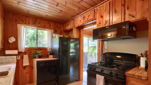A cabin-style kitchen with wooden walls, a black refrigerator, a stove, and a dishwasher.