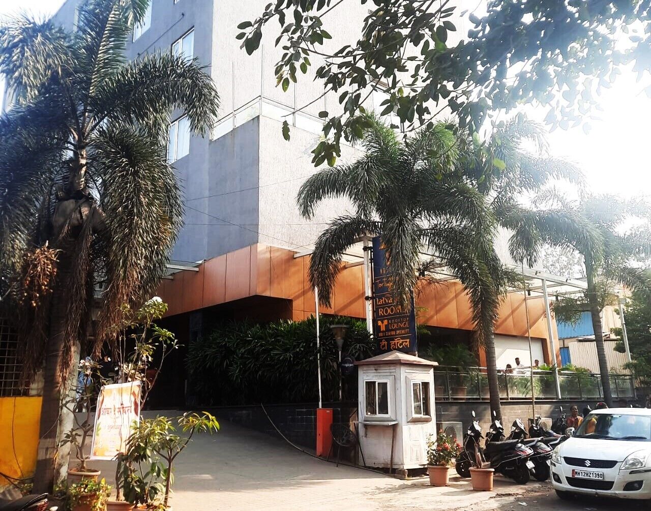 A modern building with a prominent entrance, a small security booth, and several potted plants.