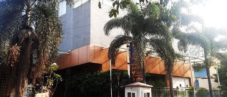 A modern building with a prominent entrance, a small security booth, and several potted plants.