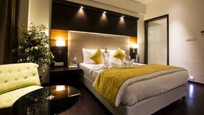 Hotellihuone, jossa on suuri sänky, napitettulla verhoilulla varustettu nojatuoli, yöpöytä ja ruukussa oleva kasvi.