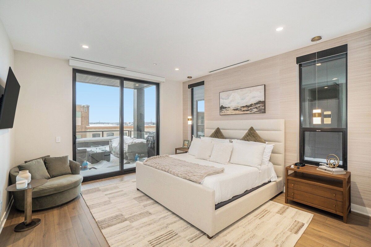 Quarto moderno com cama grande, sofá, televisão e vista para a cidade.