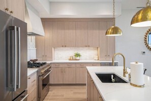 A modern kitchen with stainless steel appliances, wooden cabinets, a marble countertop, and a gold pendant light.