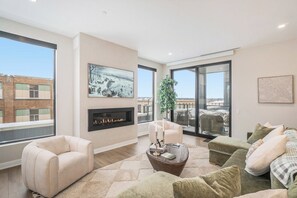 A spacious living room with a fireplace, large windows, and a view of the cityscape.