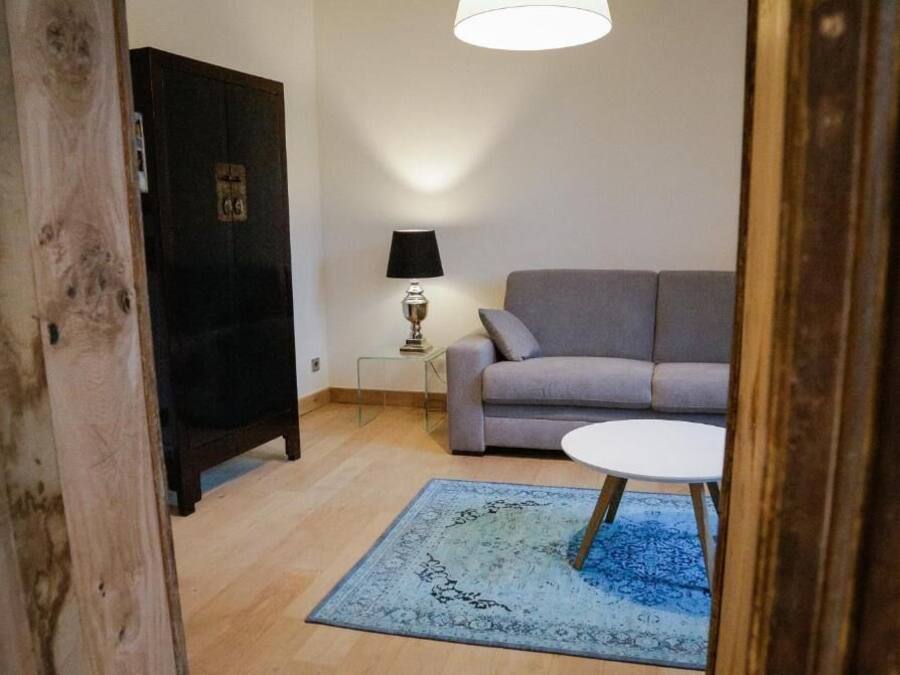Una sala de estar con un sofá gris, una mesita redonda pequeña, una lámpara y un tapete azul.