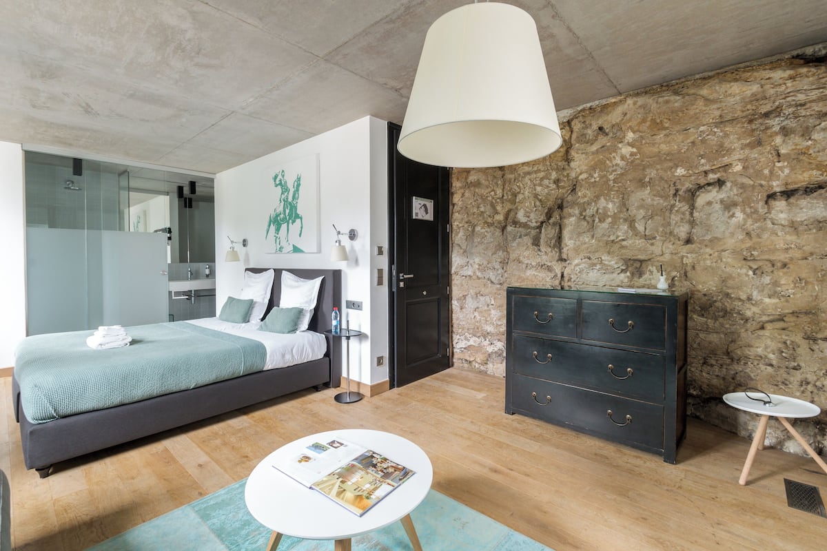 Une chambre à coucher moderne avec un lit, une table de chevet, une lampe, une commode et une petite table ronde sur laquelle repose un magazine.